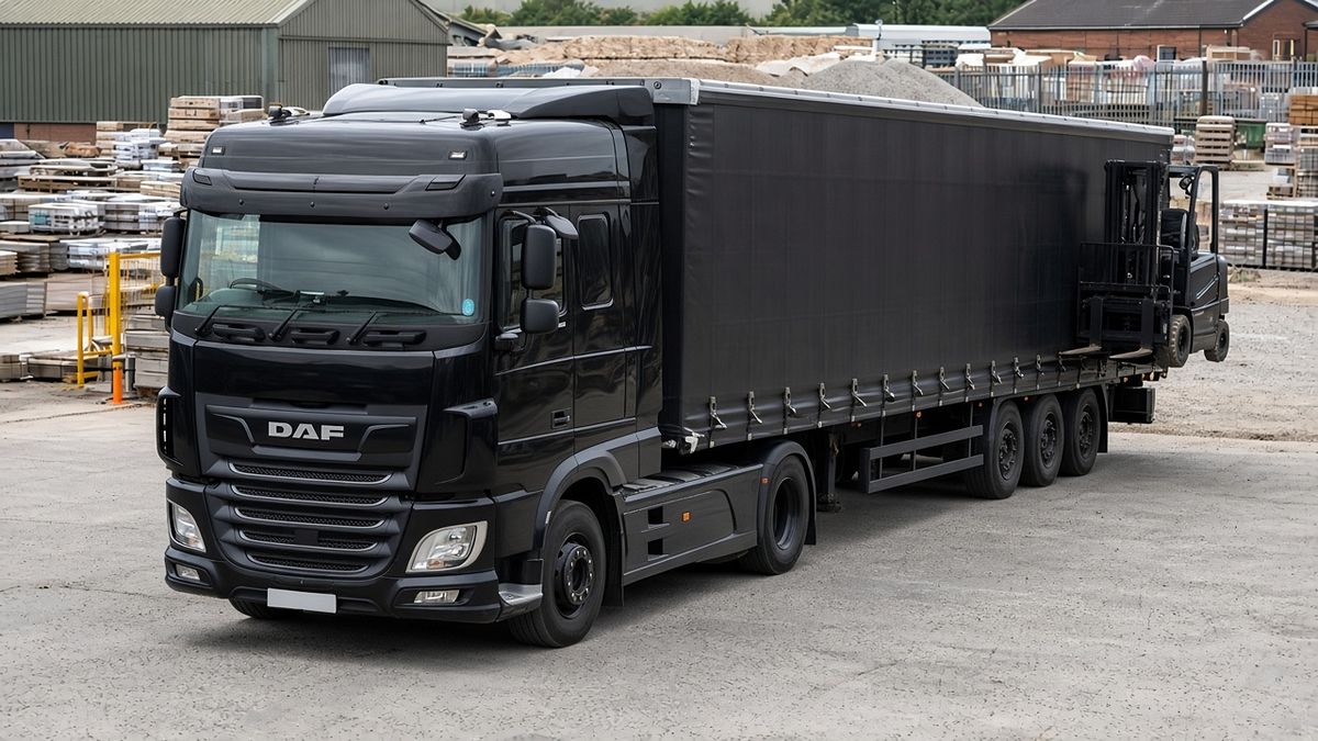 Illustrative image: plain black tractor unit and curtainsider trailer with a truck-mounted forklift on the rear at a builders’ merchant